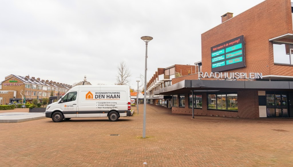 Witte bedrijfswagen van Woningontruiming Den Haan geparkeerd op het Raadhuisplein in het centrum van Rozenburg.